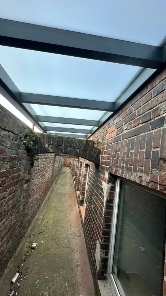 Überdachter Gang entlang einer Gebäudewand mit Gitterrostboden