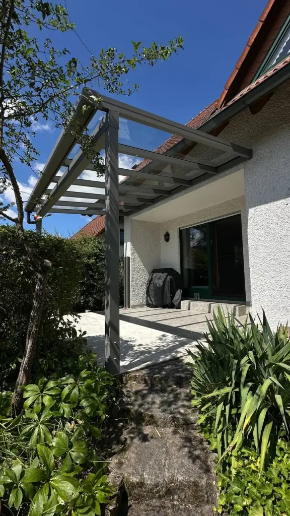 Terrassenüberdachung aus Aluminium mit Glasdach an einem hellen Haus mit Gartenweg