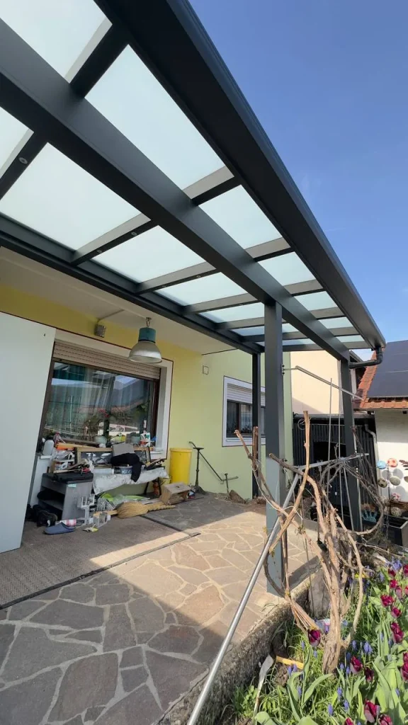 Terrassenüberdachung aus Aluminium mit Glasdach über einer Natursteinterrasse