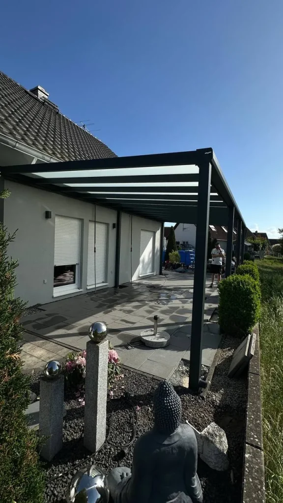 Alu-Terrassenüberdachung mit Glasdach am Haus mit Gartendekoration