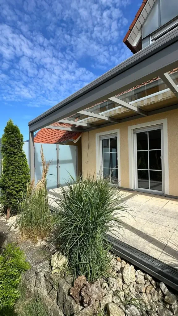 Terrassenüberdachung mit Glasdach an einer Hausecke mit Ziergräsern