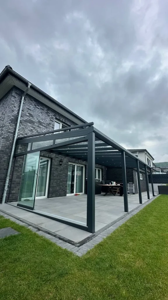 Terrassenüberdachung mit Glasdach an einem dunklen Klinkerhaus
