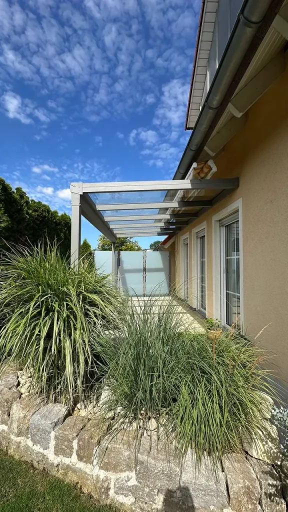 Terrassenüberdachung mit Glasdach und seitlichem Sichtschutzelement im Beet