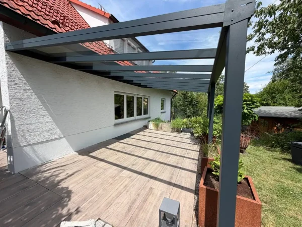 Terrassenüberdachung mit Glasdach über Holzdielen mit Blick auf das Haus