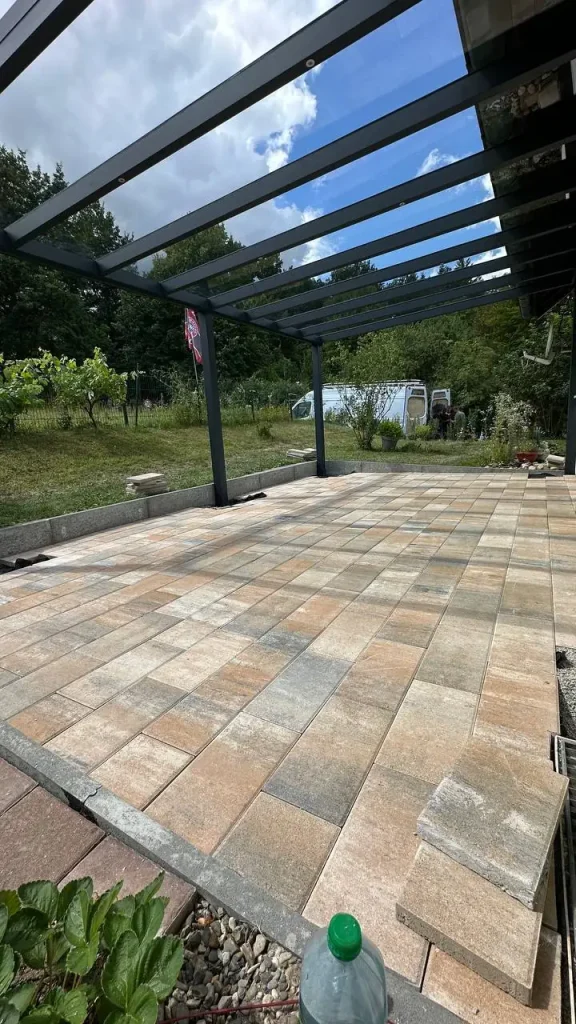 Aluminium-Terrassendach mit Glasdach über gepflasterter Terrasse im Garten