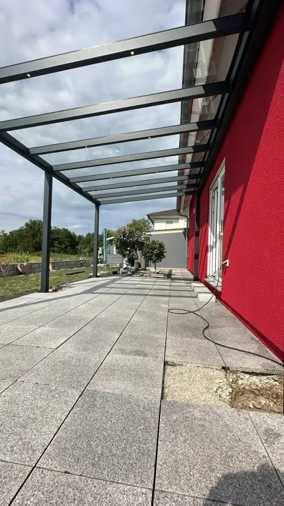 Terrassenüberdachung mit Glasdach über gepflasterter Terrasse