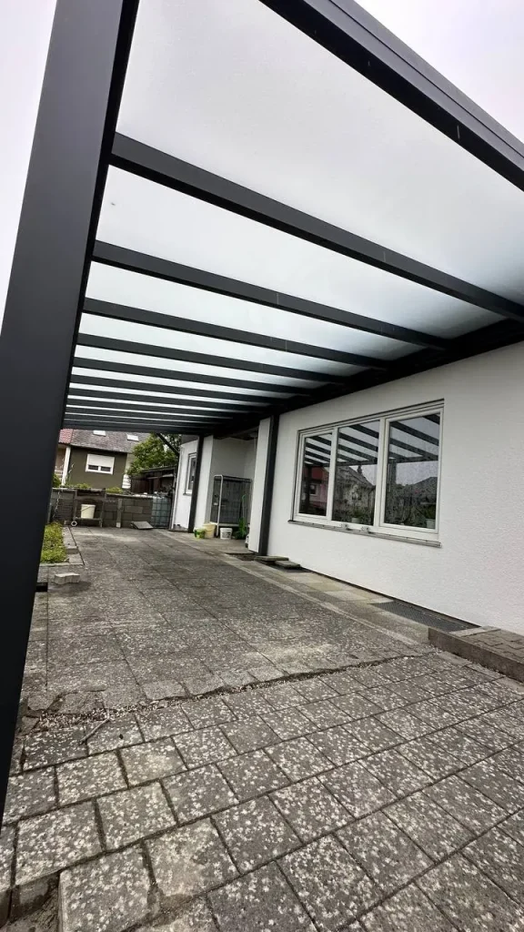Terrassenüberdachung mit Glasdach entlang der gepflasterten Einfahrt
